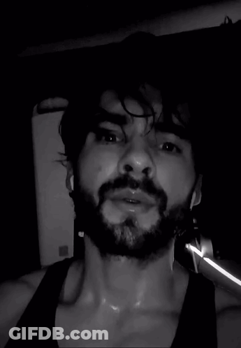 A Man With A Beard Is Sweating In A Black Tank Top . GIF