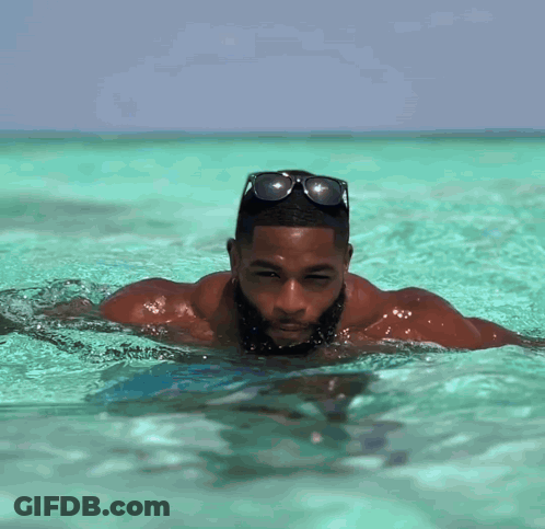 A Man With A Beard Is Swimming In The Ocean Wearing Sunglasses GIF