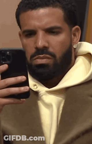 A Man With A Beard Is Taking A Picture Of Himself In A Mirror With His Cell Phone . GIF