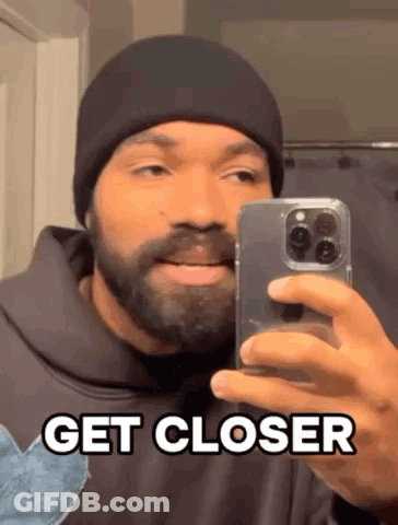 A Man With A Beard Is Taking A Selfie In Front Of A Mirror With His Phone . GIF