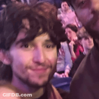 A Man With A Beard Is Taking A Selfie With Another Man In A Crowd Of People . GIF