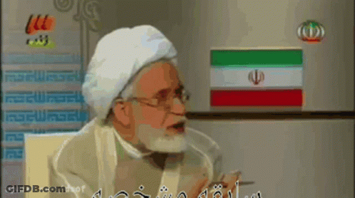 A Man With A Beard Is Talking In Front Of A Refrigerator GIF