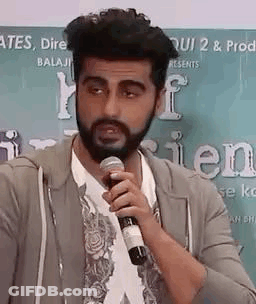 A Man With A Beard Is Talking Into A Microphone . GIF