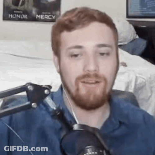 A Man With A Beard Is Talking Into A Microphone In A Room . GIF