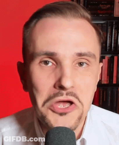 A Man With A Beard Is Talking Into A Microphone In Front Of A Bookshelf Filled With Books . GIF