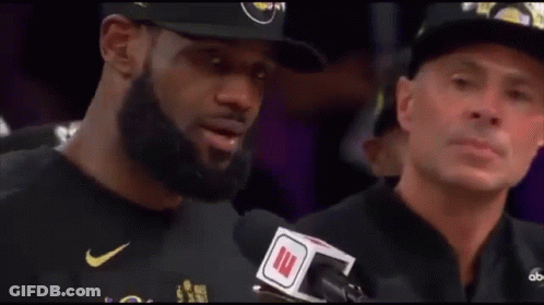 A Man With A Beard Is Talking Into A Microphone While Another Man Watches . GIF
