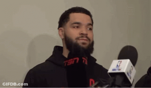 A Man With A Beard Is Talking Into A Microphone While Wearing A Black Hoodie . GIF
