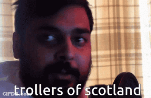 A Man With A Beard Is Talking Into A Microphone With The Words " Trollers Of Scotland " Written Below Him GIF
