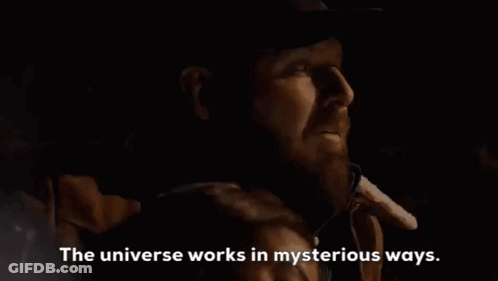 A Man With A Beard Is Talking On A Cell Phone In A Dark Room With The Words `` The Universe Works In Mysterious Ways '' GIF