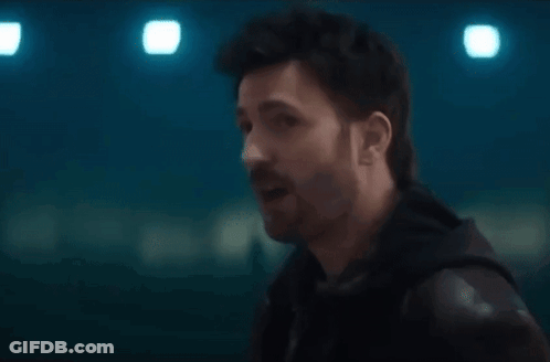 A Man With A Beard Is Talking To Another Man In A Dark Room . GIF