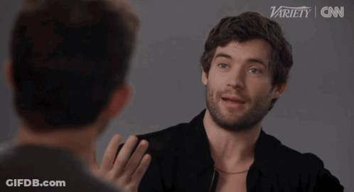 A Man With A Beard Is Talking To Another Man In Front Of A Variety Logo GIF