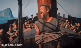 A Man With A Beard Is Tied To A Pole In Front Of A Boat GIF