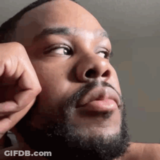 A Man With A Beard Is Touching His Face With His Hand And Looking Up . GIF
