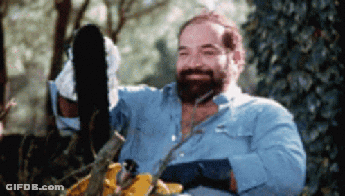 A Man With A Beard Is Using A Chainsaw To Cut A Tree Branch GIF
