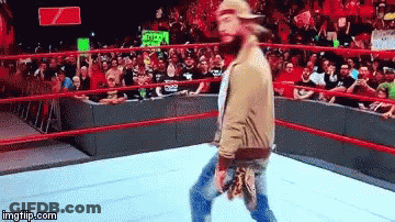 A Man With A Beard Is Walking In A Wrestling Ring With A Crowd Behind Him . GIF