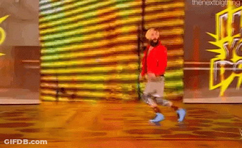 A Man With A Beard Is Walking On A Wooden Floor In Front Of A Wall With Graffiti On It . GIF