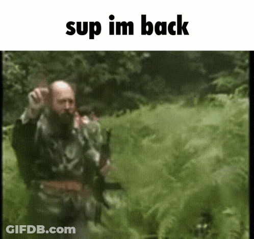 A Man With A Beard Is Walking Through A Grassy Field With The Words " Sup Im Back " Above Him GIF