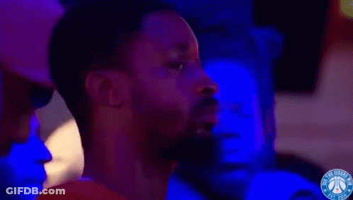 A Man With A Beard Is Watching A Basketball Game In A Dark Room With Blue Lights . GIF