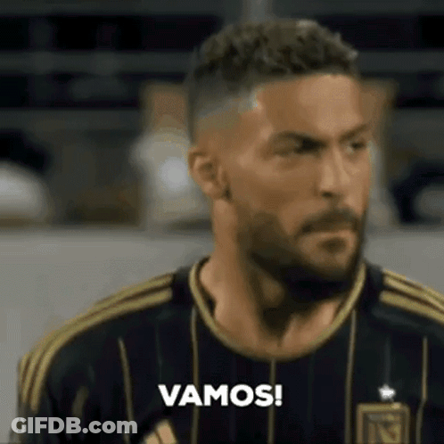 A Man With A Beard Is Wearing A Black And Gold Jersey And Says Vamos ! GIF