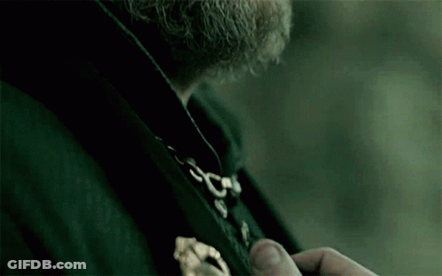 A Man With A Beard Is Wearing A Black Coat With A Gold Buckle . GIF