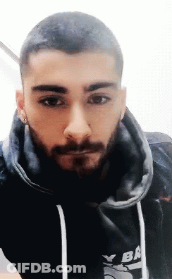 A Man With A Beard Is Wearing A Black Hoodie And Earrings . GIF