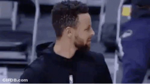 A Man With A Beard Is Wearing A Black Hoodie And Standing In Front Of A Basketball Court . GIF