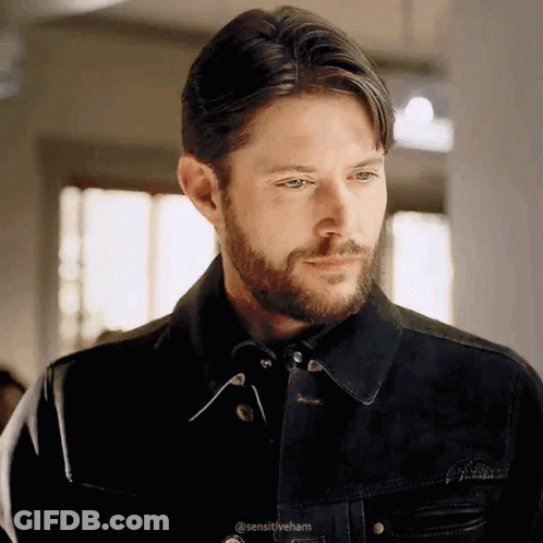 A Man With A Beard Is Wearing A Black Jacket And Looking At Something . GIF