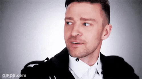 A Man With A Beard Is Wearing A Black Jacket And White Shirt And Making A Funny Face . GIF