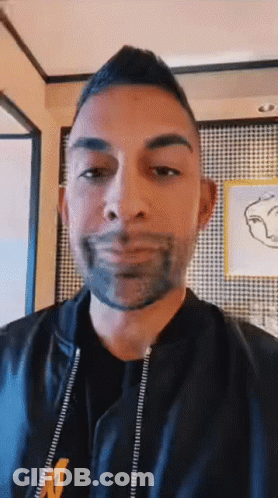 A Man With A Beard Is Wearing A Black Jacket With The Letter M On The Front GIF