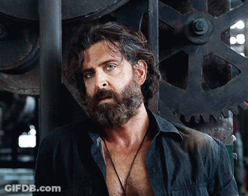 A Man With A Beard Is Wearing A Black Shirt And A Necklace GIF