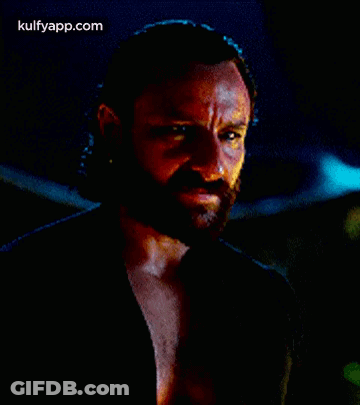 A Man With A Beard Is Wearing A Black Shirt And Looking At The Camera . GIF