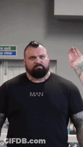 A Man With A Beard Is Wearing A Black Shirt That Says Man On It GIF