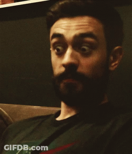 A Man With A Beard Is Wearing A Black Shirt With A Green Circle On It GIF