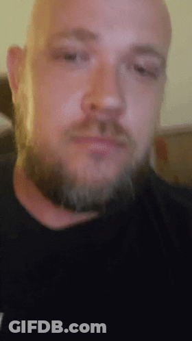 A Man With A Beard Is Wearing A Black Shirt With A T On It GIF