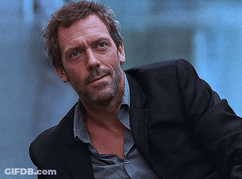 A Man With A Beard Is Wearing A Black Suit And A Grey Shirt GIF