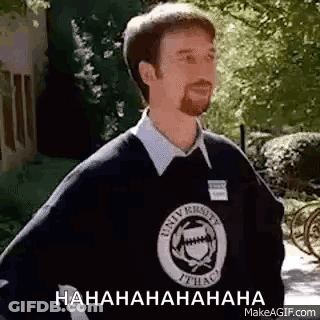 A Man With A Beard Is Wearing A Black Sweater And A White Shirt And Is Laughing . GIF