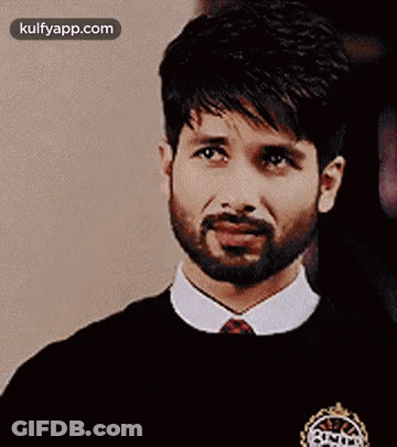 A Man With A Beard Is Wearing A Black Sweater And A White Shirt And Tie . GIF