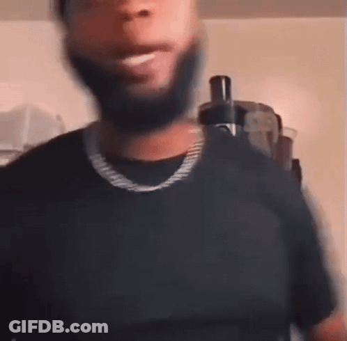 A Man With A Beard Is Wearing A Black T-Shirt And A Gold Chain Around His Neck . GIF