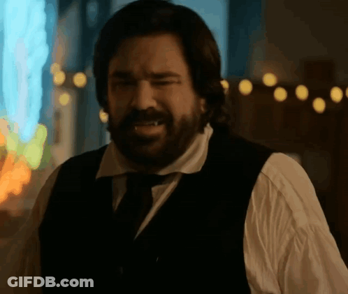 A Man With A Beard Is Wearing A Black Vest And Tie . GIF