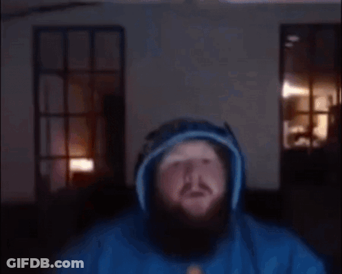 A Man With A Beard Is Wearing A Blue Hoodie And Headphones And Giving A Thumbs Up . GIF