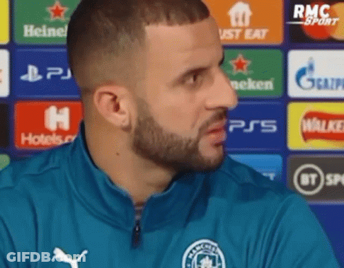 A Man With A Beard Is Wearing A Blue Jacket And Talking To A Reporter . GIF