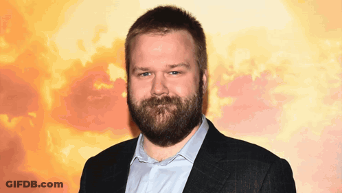 A Man With A Beard Is Wearing A Blue Shirt And A Black Jacket GIF