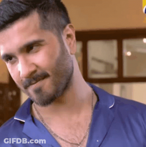 A Man With A Beard Is Wearing A Blue Shirt And A Necklace . GIF