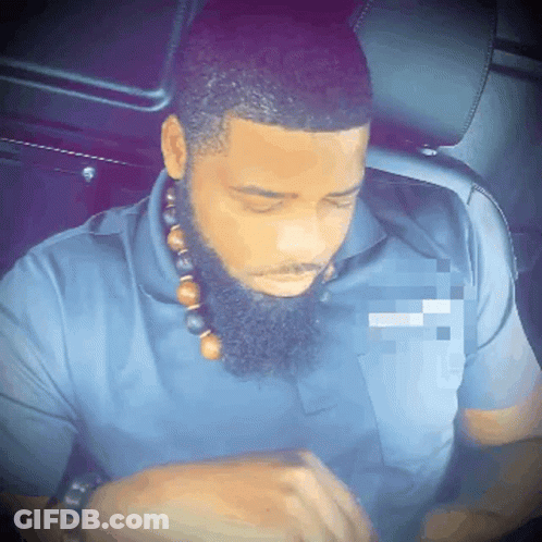 A Man With A Beard Is Wearing A Blue Shirt And A Necklace With Beads Around His Neck GIF