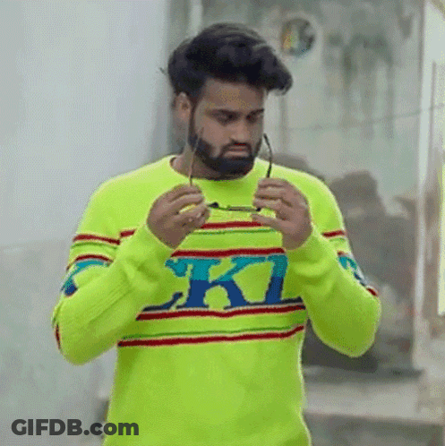 A Man With A Beard Is Wearing A Bright Yellow Sweater And Holding Glasses . GIF