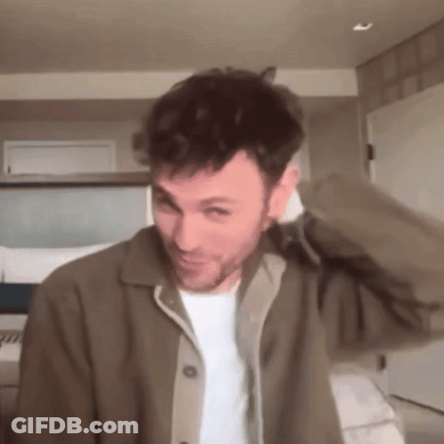 A Man With A Beard Is Wearing A Brown Jacket And White Shirt GIF