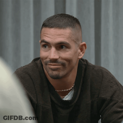 A Man With A Beard Is Wearing A Brown Sweater And A Gold Chain Around His Neck GIF