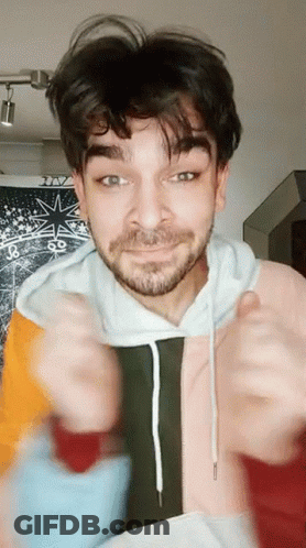 A Man With A Beard Is Wearing A Colorful Hoodie And Giving A Thumbs Up Sign GIF