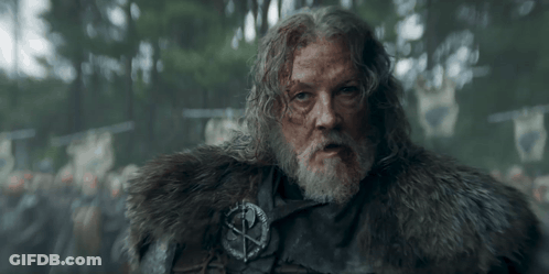 A Man With A Beard Is Wearing A Fur Coat And A Badge With A Cross On It . GIF