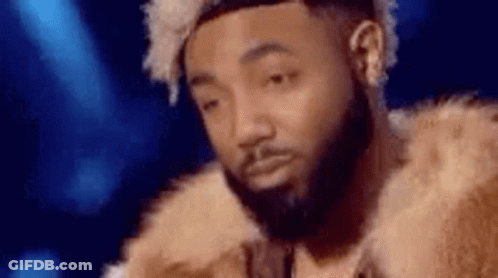A Man With A Beard Is Wearing A Fur Coat And Making A Funny Face . GIF